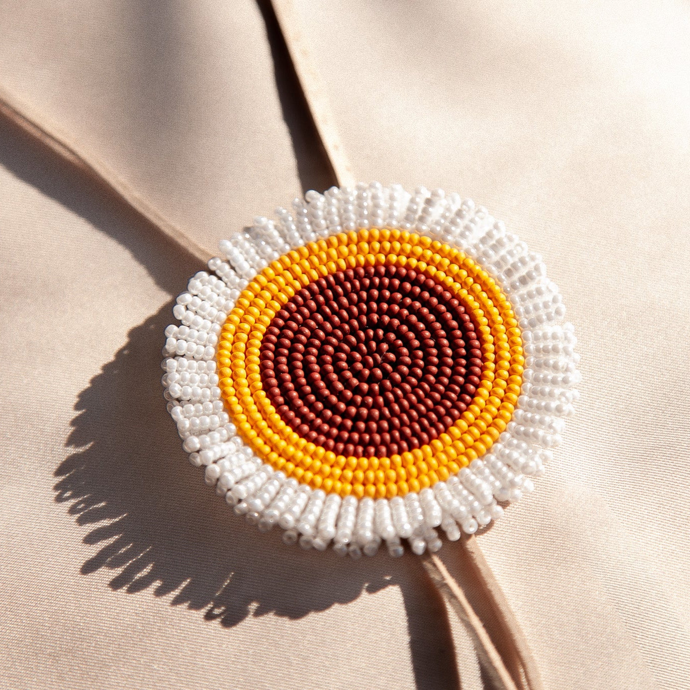 Beaded brooch with concentric circles in white, yellow, and brown on a beige fabric background